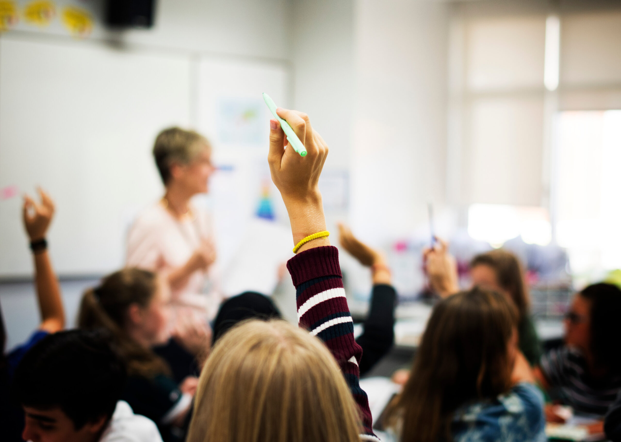 Students with their hands up responding to their teacher.