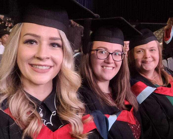 Three women in graduation gowns and caps, smiling at the camera.